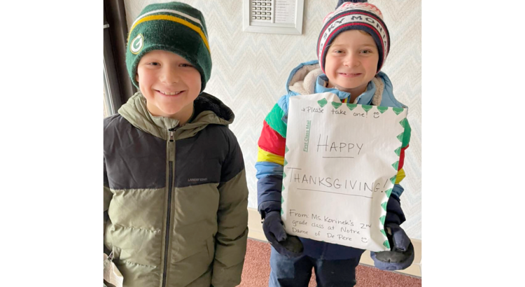 Students from Notre Dame of De Pere school with a happy thanksgiving sign in winterwear.